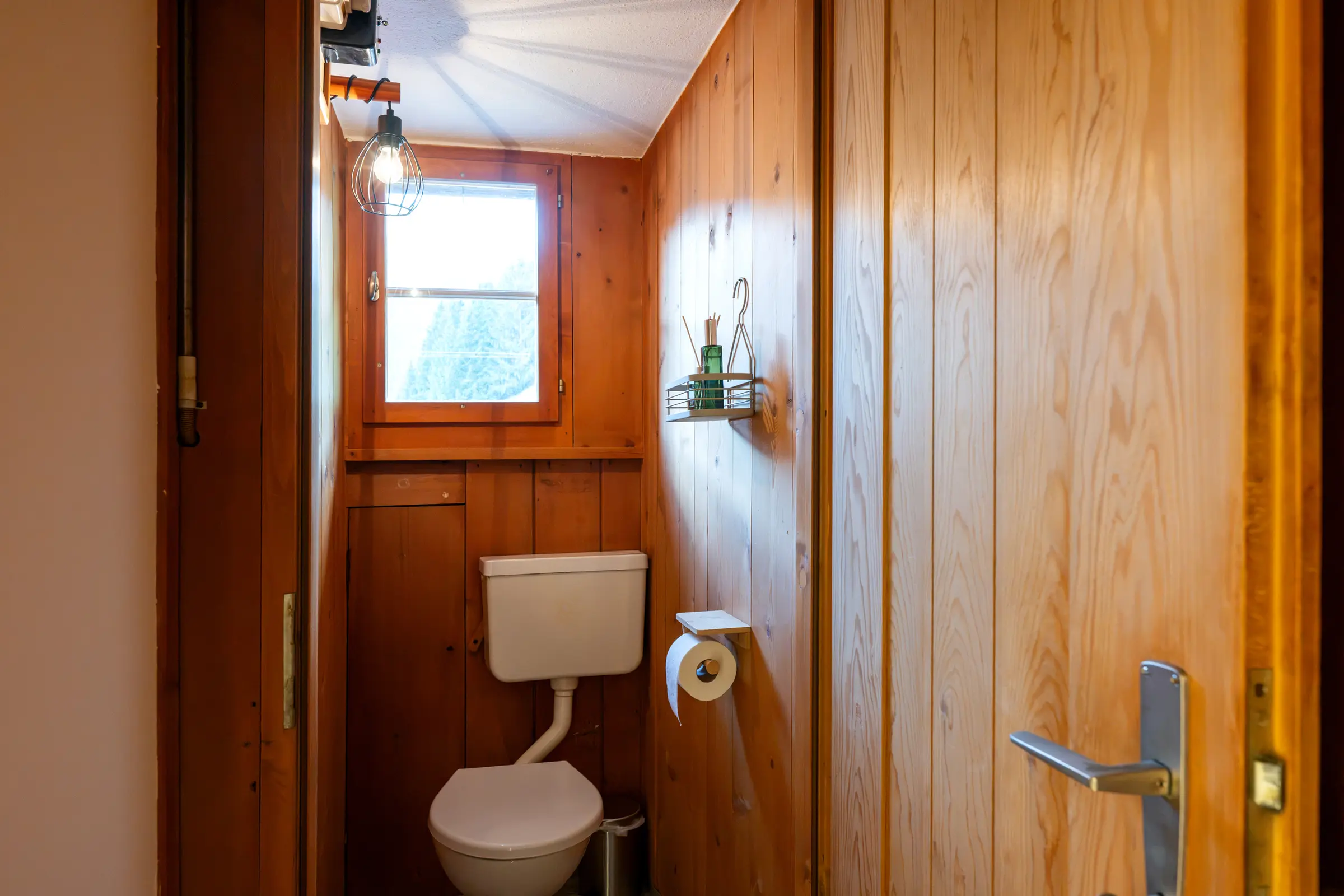 The separate WC with wood panelling and a small window, beside it the open door with its handle.