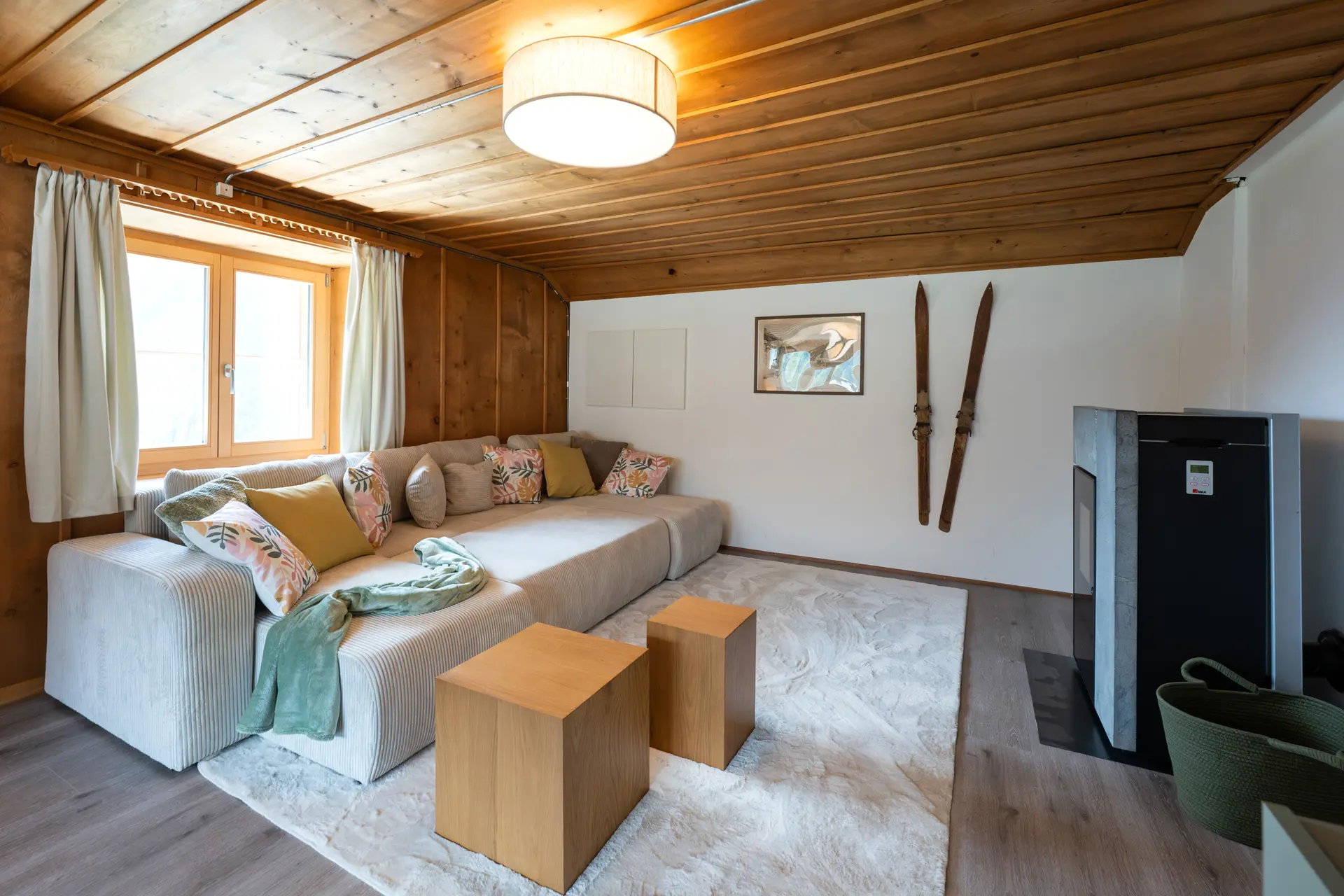 Living room of the 9° Ost holiday flat with Swiss pine on walls and ceiling, a pellet stove and old skis on the wall
